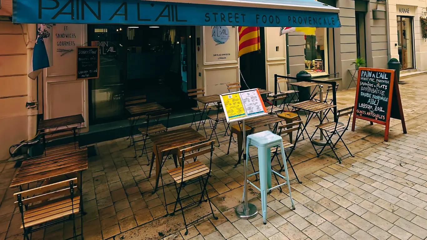 Terrasse du restaurant Pain à l’Ail à Marseille, spécialisé en street food provençale, avec tables extérieures, ardoise de menu et store bleu.